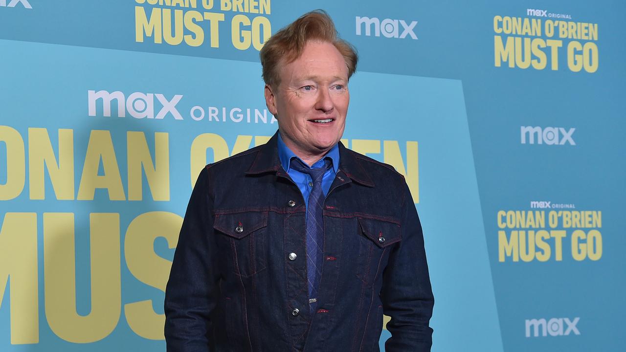 Conan O'Brien steht vor einer Werbetafel.