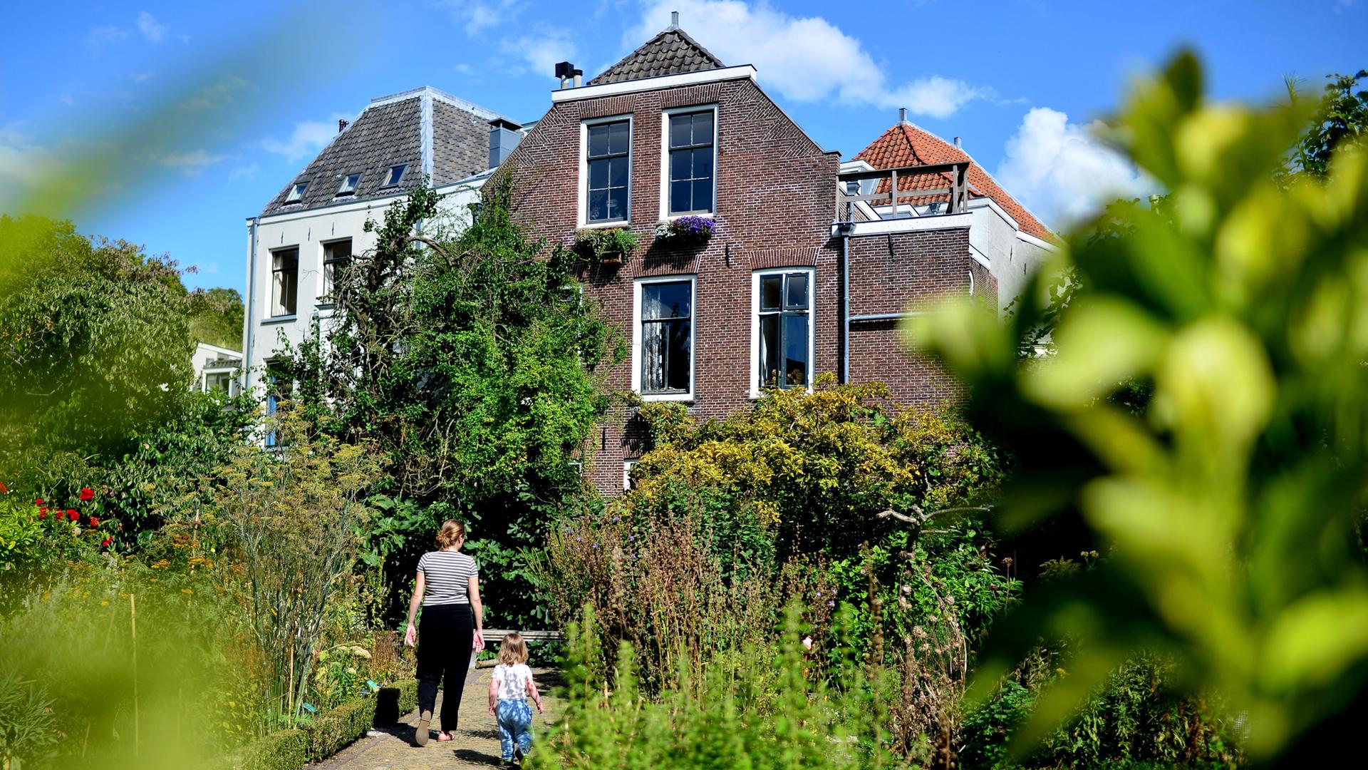 Mutter und Kind laufen über einen Gartenweg auf ein Haus zu