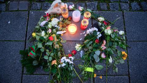 Kerzen und Blumen umgeben eine Gedenkplatte im Gehweg, die an ein Opfer des Anschlags auf den Magdeburger Weihnachtsmarkt erinnert. 
