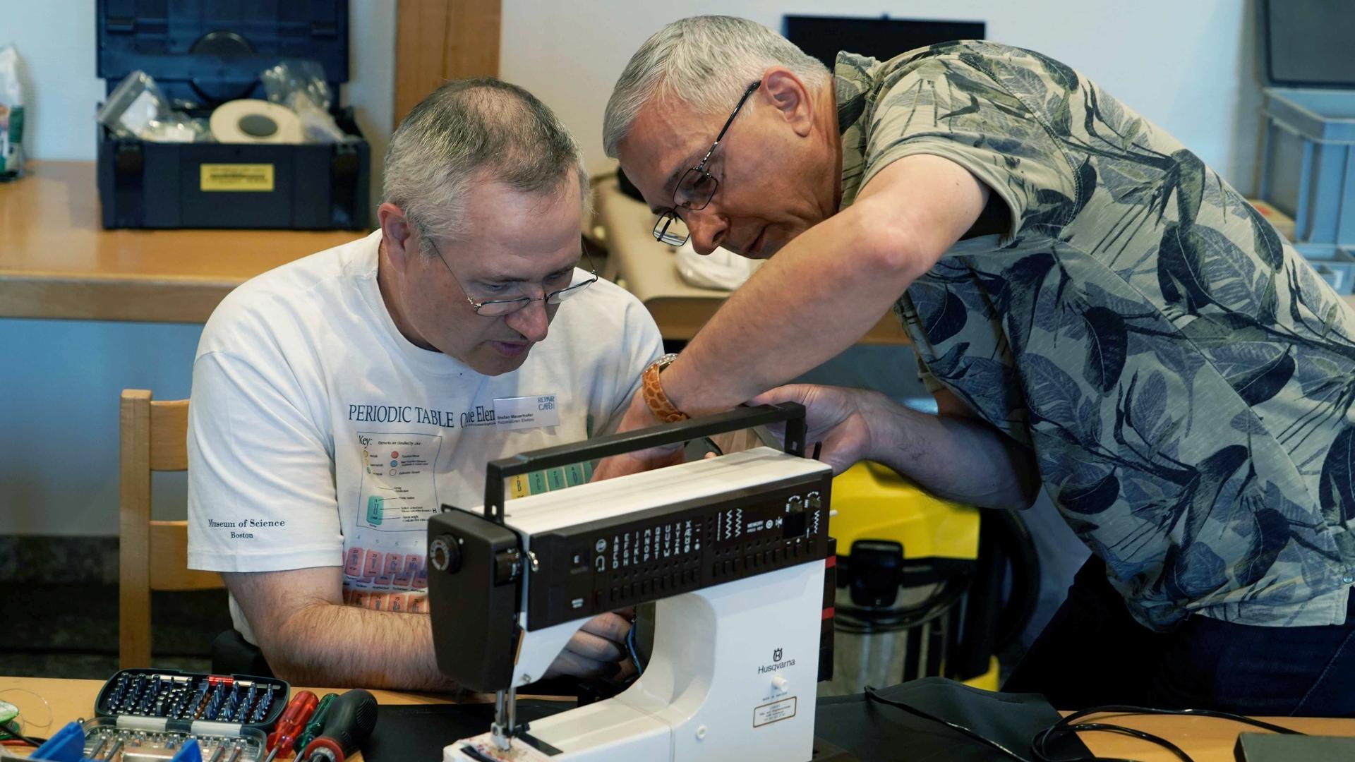 Zwei Mitarbeiter eines Repair-Cafes reparieren eine Nähmaschine.