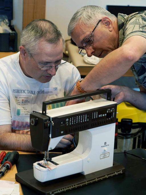 Zwei Mitarbeiter eines Repair-Cafes reparieren eine Nähmaschine.
