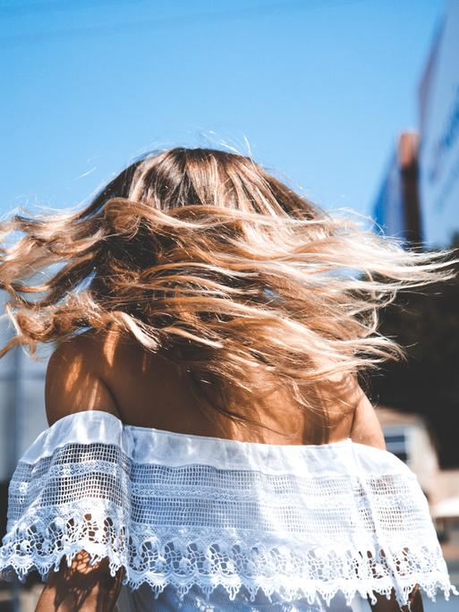 Eine Frau mit blonden Haaren läuft durch die Gegend. Wir sehen sie von hinten. 