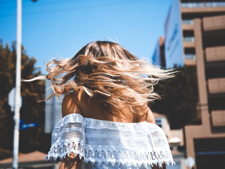 Eine Frau mit blonden Haaren läuft durch die Gegend. Wir sehen sie von hinten. 