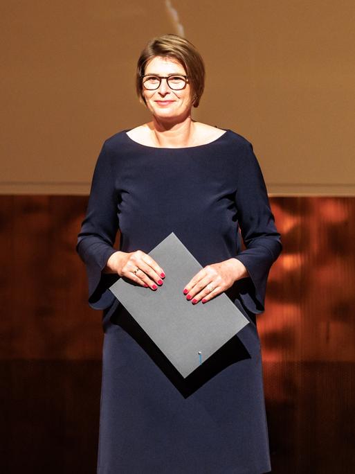 Eine Frau steht im Abendkleid auf einer Bühne und freut sich.