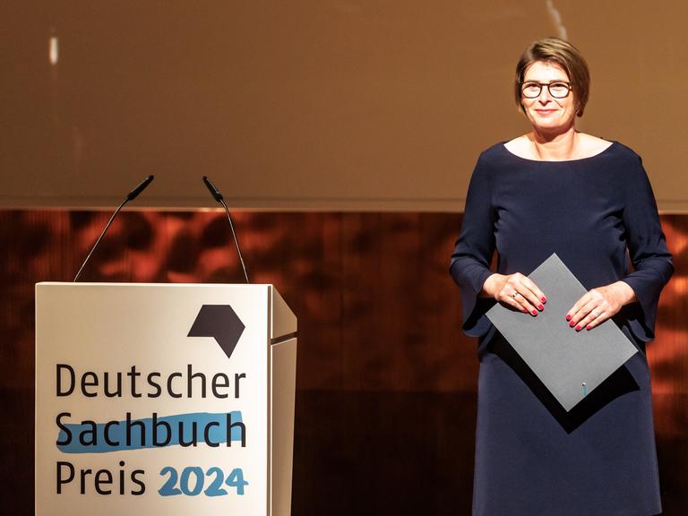 Eine Frau steht im Abendkleid auf einer Bühne und freut sich.