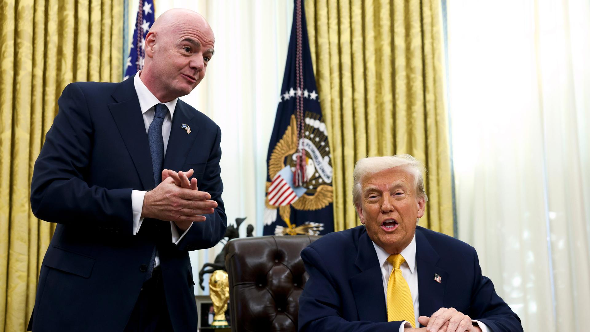 Im Oval Office: Trump sitzt, Infantino steht neben ihm. Beide tragen dunkle Jacketts. Dahinter ein Fenster mit Gardinen