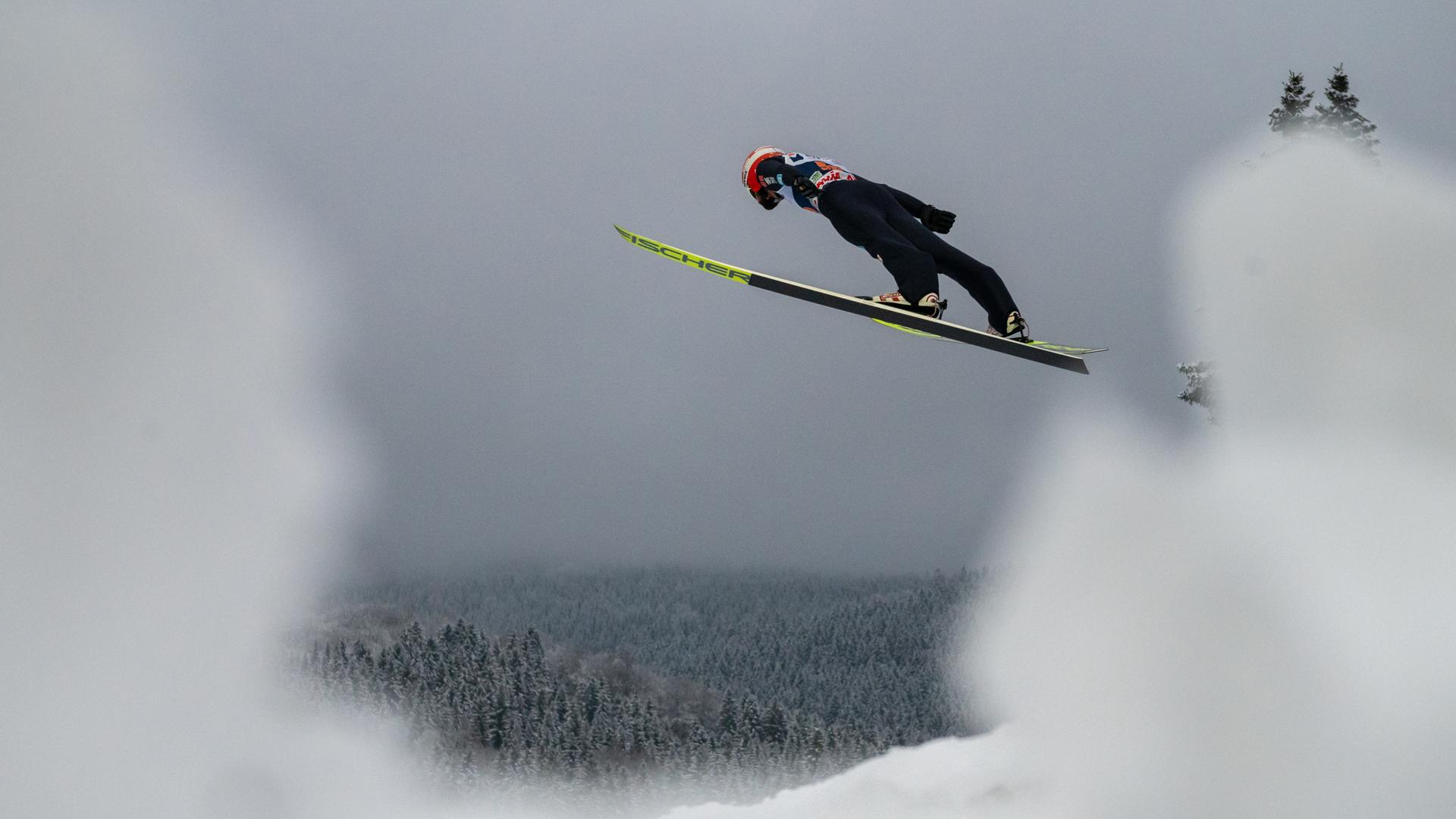 Markus Eisenbichler fliegt vor dem Hintergrund aus Wald und Schnee.