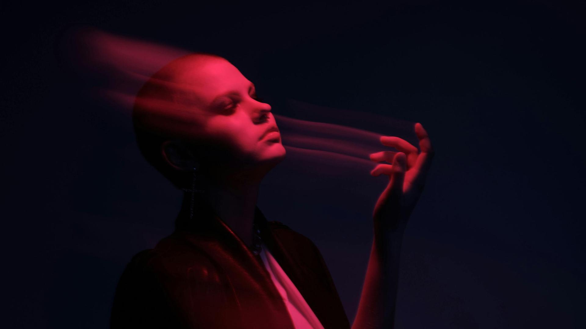 Das Gesicht einer Frau ist verschwommen in ihrer Pose im rosafarbenem Licht.