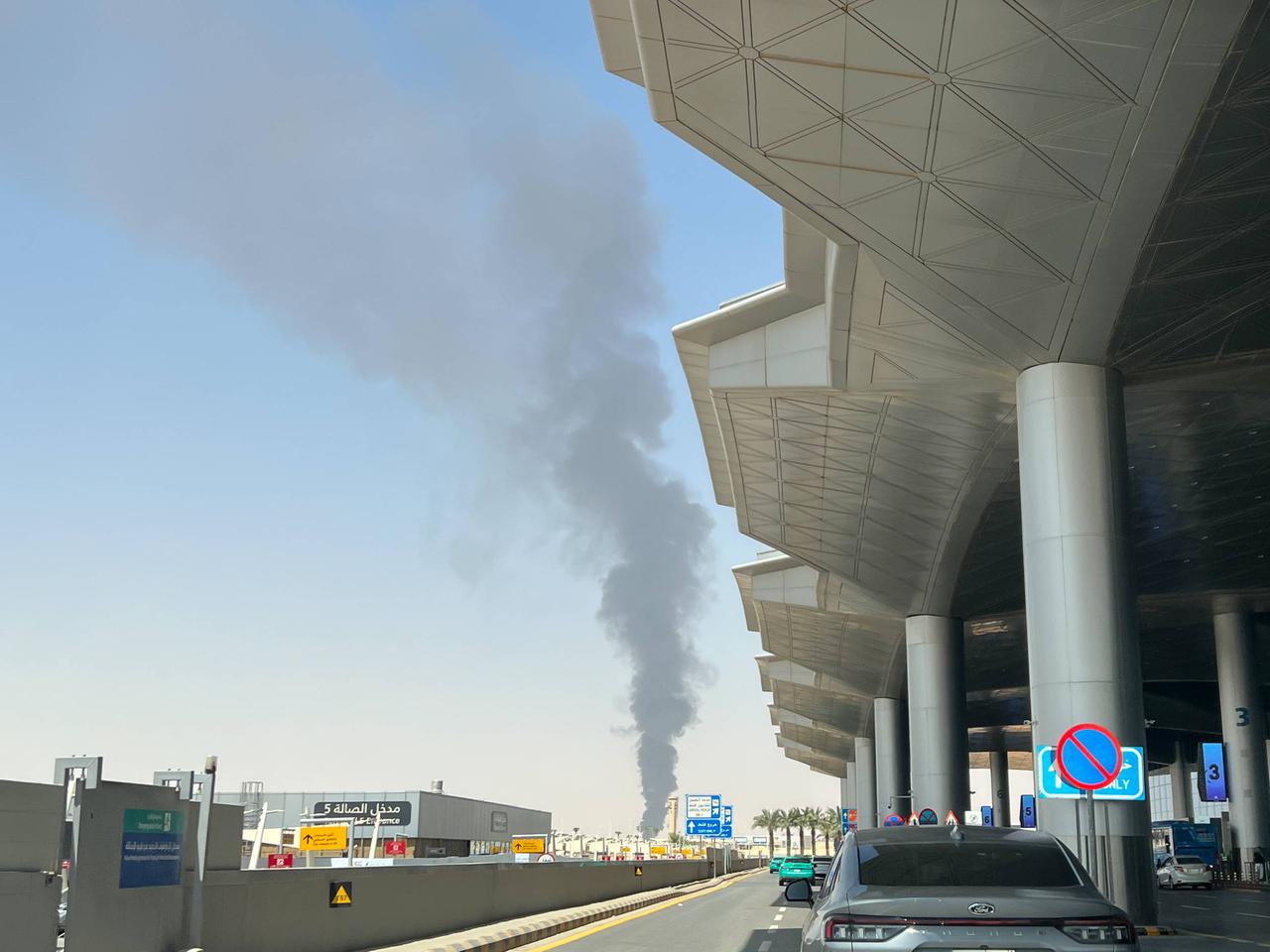 Hinter dem Gebäude am internationalen Flughafen in Saudi-Arabien steigt eine schwarze Rauchsäule in den blauen Himmel.
