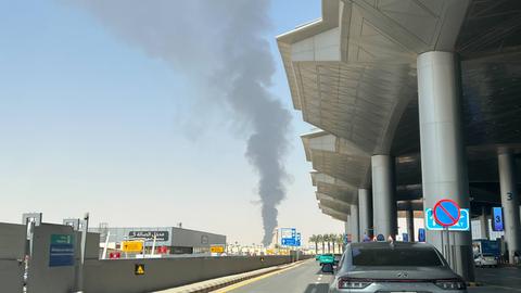 Hinter dem Gebäude am internationalen Flughafen in Saudi-Arabien steigt eine schwarze Rauchsäule in den blauen Himmel.