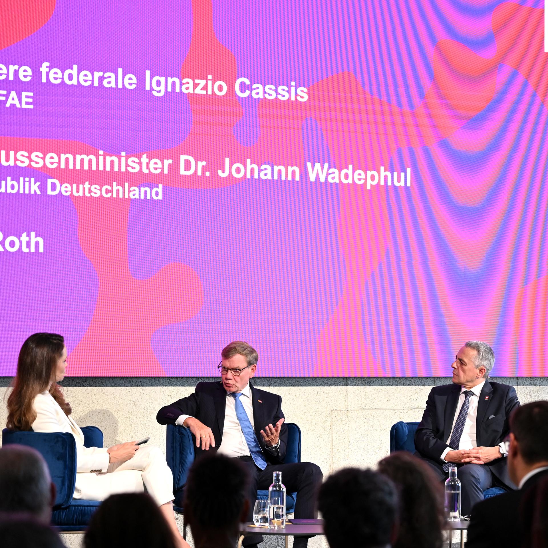 Johann Wadephul (M., CDU), Außenminister, der schweizerische Vorsteher desEidgenössischen Departements für auswärtigen Angelegenheiten, Ignazio Cassis (r), und Moderatorin Carolin Roth bei einer gemeinsamen Panel-Diskussion im Bernexpo Cube.