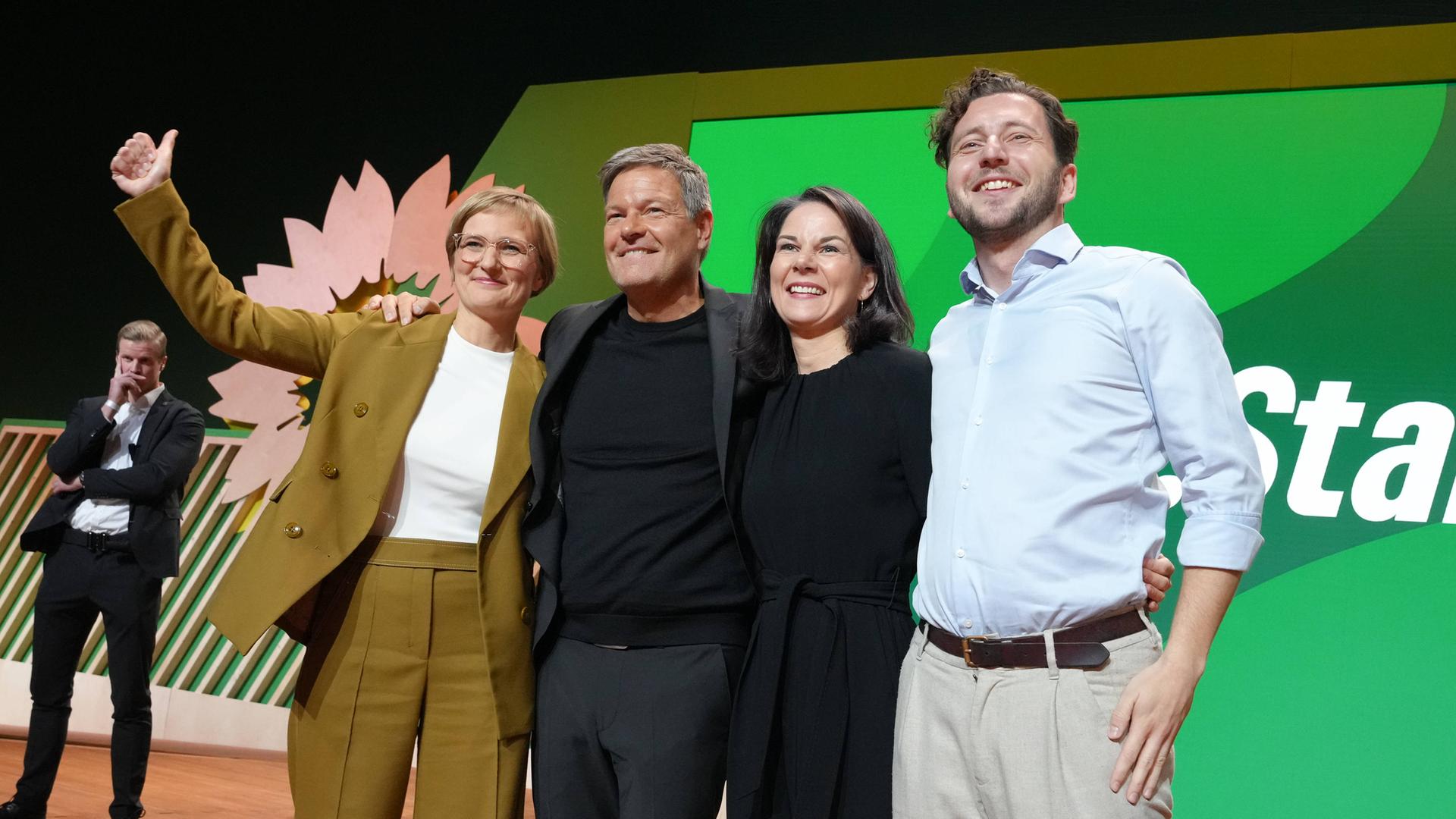 Felix Banaszak, Annalena Baerbock, Robert Habeck und Franziska Brantner jubeln gemeinsam auf einer Bühne bei der 50. Bundesdelegiertenkonferenz der Grünen in Wiesbaden.