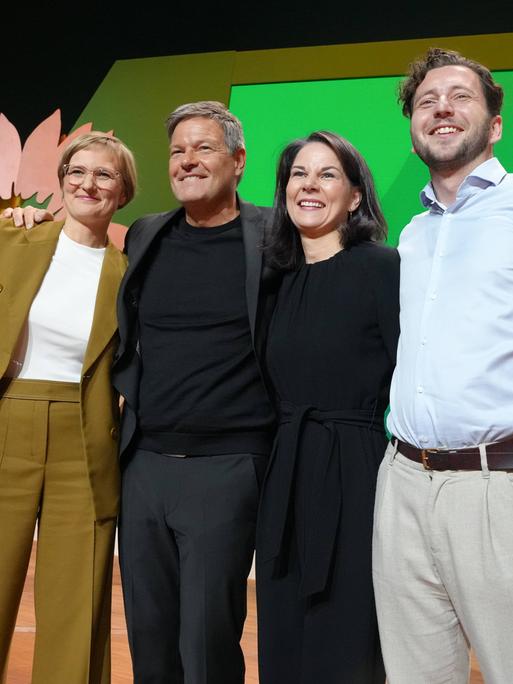 Felix Banaszak, Annalena Baerbock, Robert Habeck und Franziska Brantner jubeln gemeinsam auf einer Bühne bei der 50. Bundesdelegiertenkonferenz der Grünen in Wiesbaden.