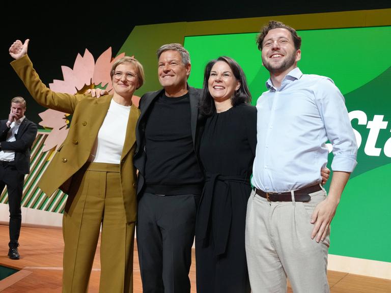 Felix Banaszak, Annalena Baerbock, Robert Habeck und Franziska Brantner jubeln gemeinsam auf einer Bühne bei der 50. Bundesdelegiertenkonferenz der Grünen in Wiesbaden.