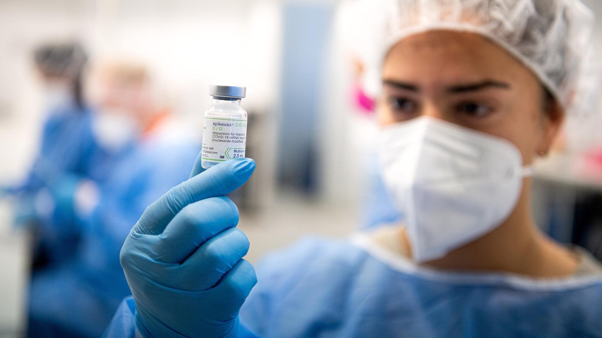 Mitarbeiterin hält eine Flasche mit Impfstoff hoch (Symbolbild) 