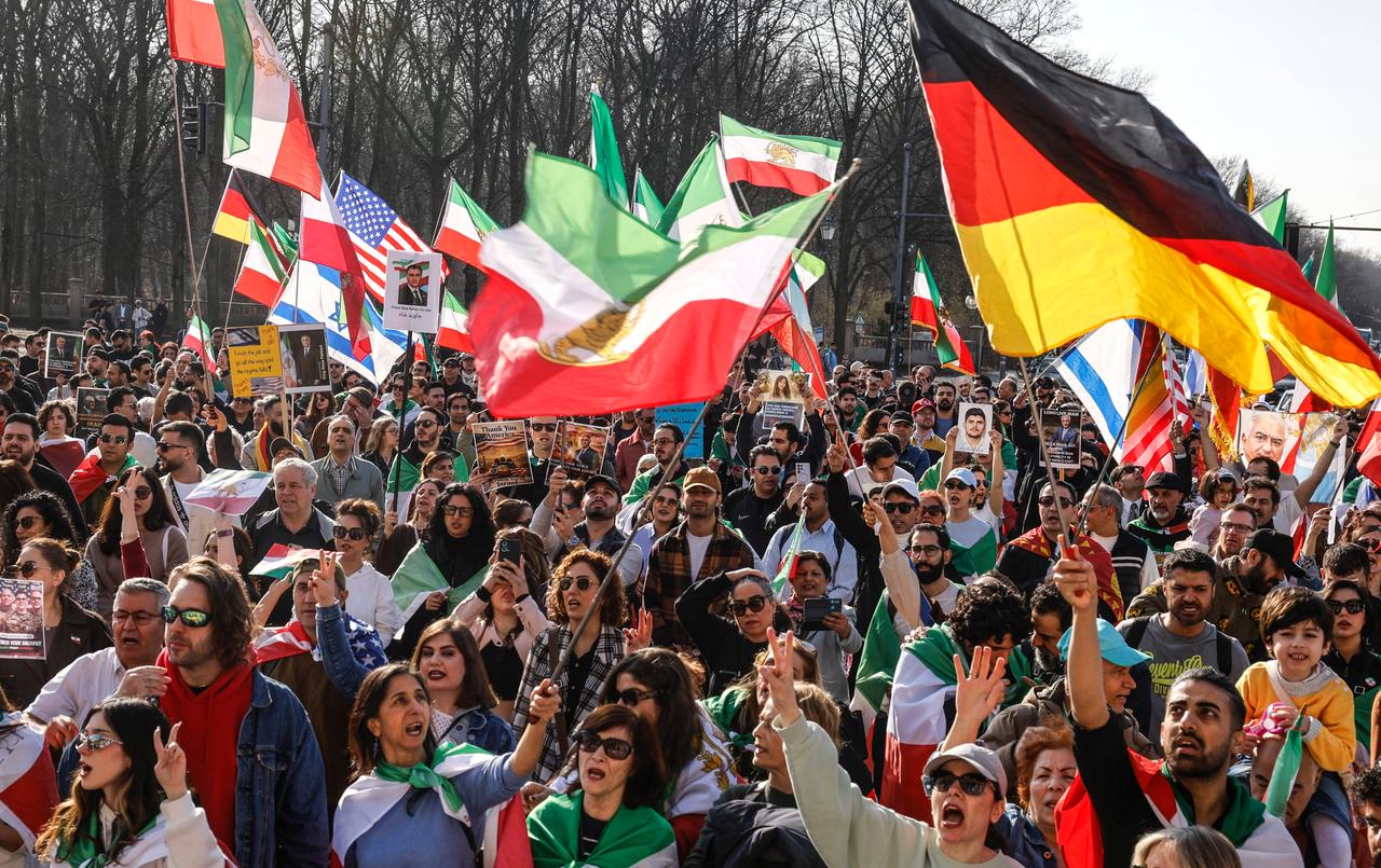 Menschen stehen in Berlin mit deutschen, israelischen, iranischen und amerikanischen Flaggen und Plakaten von Prinz Reza Pahlavi zusammen.