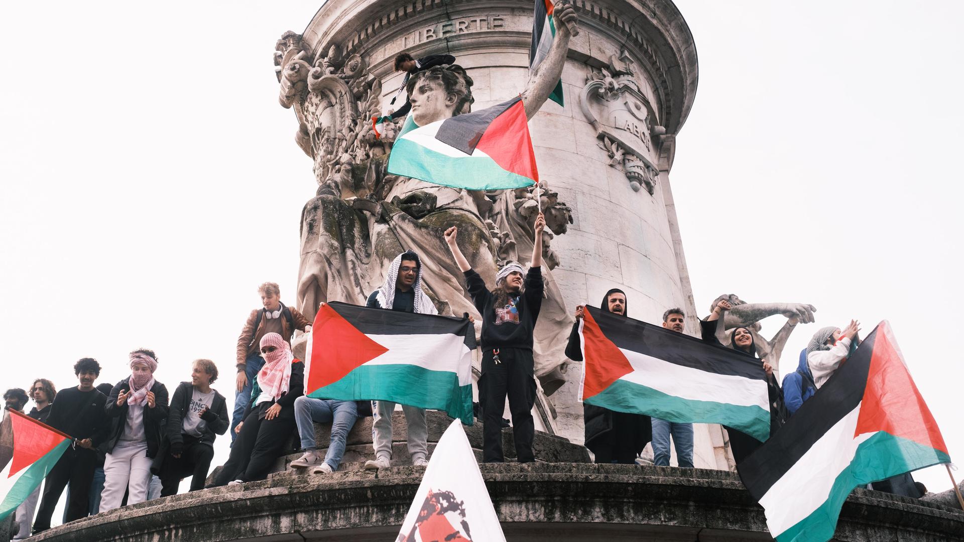 Demonstranten stehen in Paris auf dem Sockel einer Säule und halten Palästinenserflaggen hoch. 