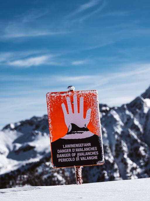 Ein rotes Schild mit einer erhobenen Hand warnt Skifahrer vor einer Bergkulisse vor der Lawinengefahr.
