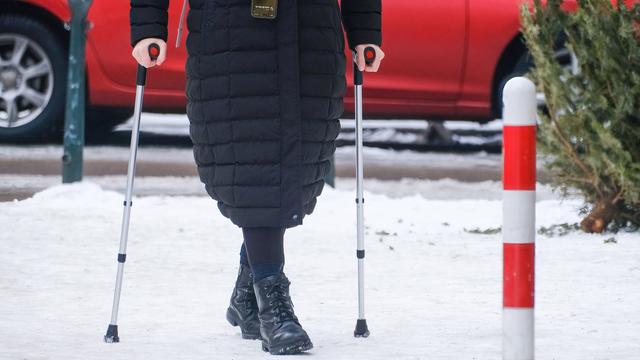 Eine Person an Krücken in Winter-Kleidung geht auf einer verschneiten Straße.