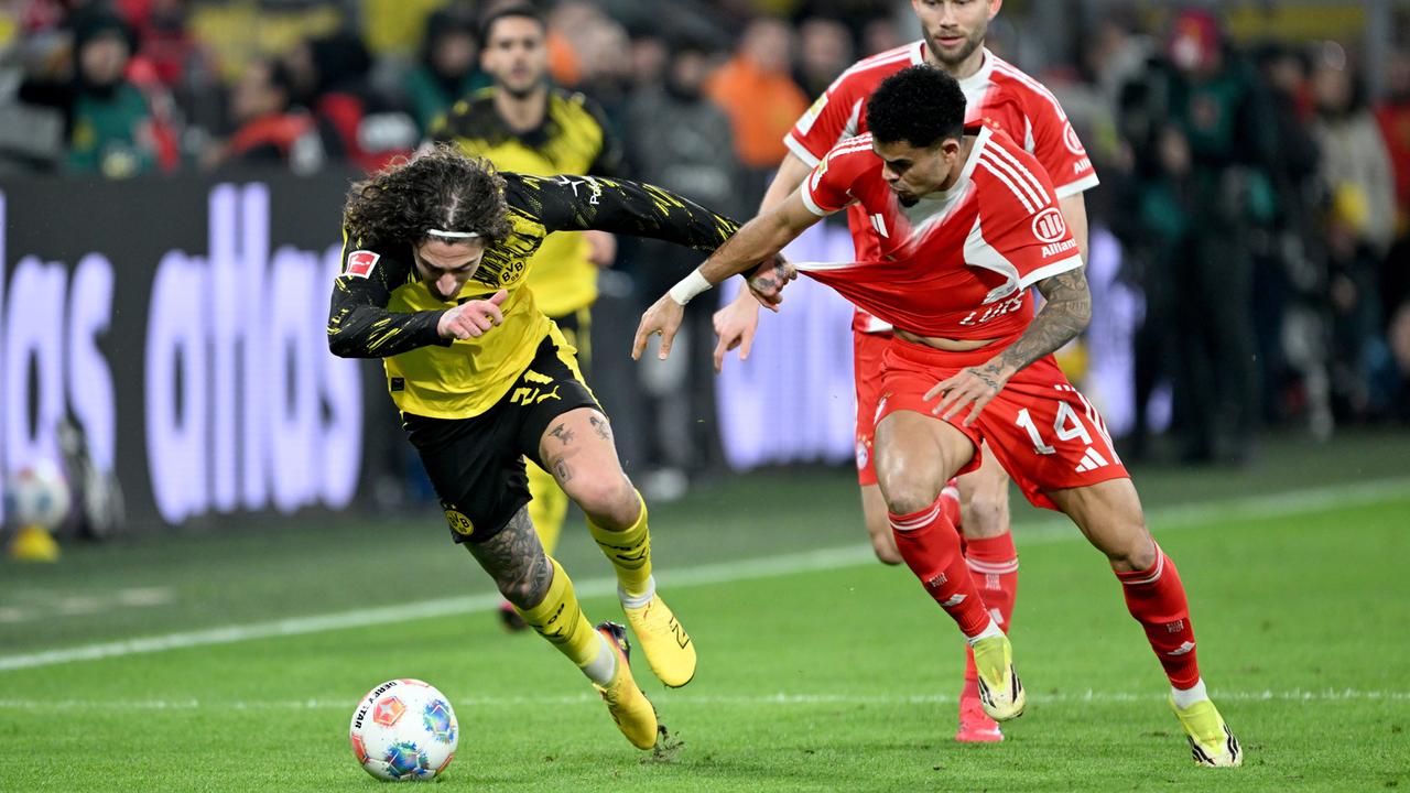 Das Bild zeigt einen Zweikampf um den Ball zwischen Fußballern mit rot-weißen Müchner und gelb-schwarzen Dortmunder Trikots.