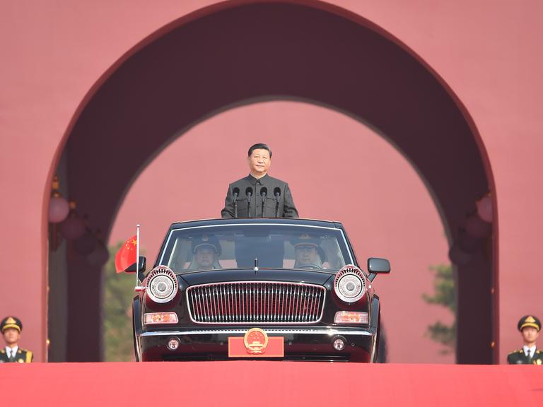 Der chinesische Staatspräsident Xi Jingping wird in einer offenen, schwarzen Limousine stehend von zwei Fahrern gefahren
