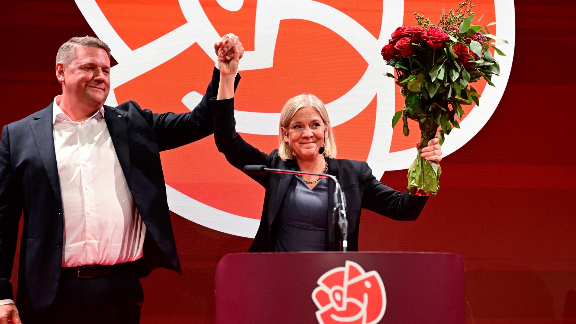 Tobias Baudin, Parteisekretär der Sozialdemokraten, und Parteivorsitzende Magdalena Andersson halten die erhobenen Hände und einen Strauß Rosen in die Höhe