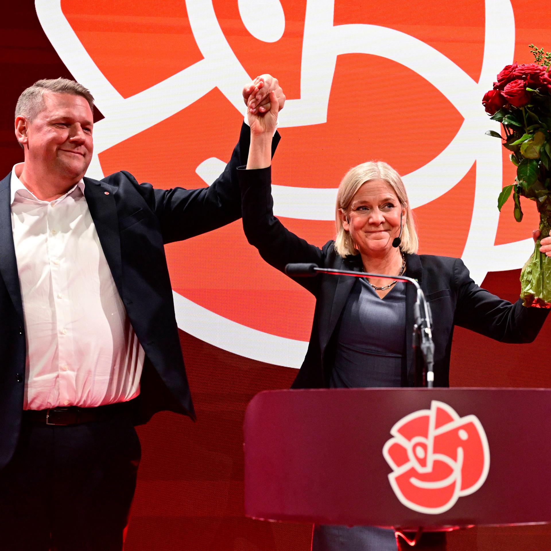 Tobias Baudin, Parteisekretär der Sozialdemokraten, und Parteivorsitzende Magdalena Andersson halten die erhobenen Hände und einen Strauß Rosen in die Höhe