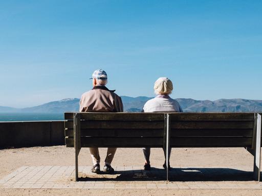 Zwei Menschen im Rentenalter sitzen auf einer Parkbank