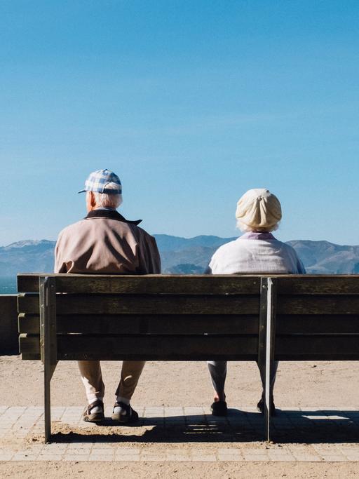Zwei Menschen im Rentenalter sitzen auf einer Parkbank