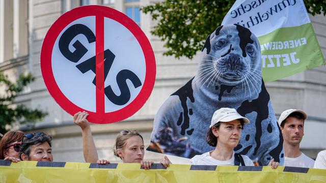 Demonstranten halten mehrere Schilder hoch, darunter ein Stoppschild mit der zusätzlichen Aufschrift Gas und das Bild einer ölverschmierten Robbe. Vor ihnen ist ein Transparent zu sehen, auf dem steht: "Keine neuen Gasbohrungen."