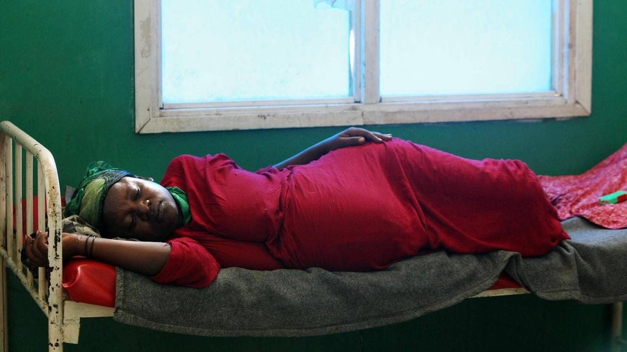 Eine schwangere Frau liegt auf der Seite auf einem Bett in Somalia. Eine schwangere Frau liegt auf der Seite auf einem Bett in Somalia.