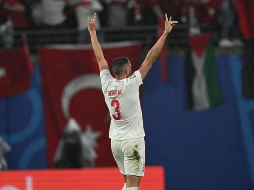 Der türkische Nationalaspieler Merih Demiral steht mit dem Rücken zur Kamera. Er zeigt mit beiden Händen den Wolfsgruß: Mittel- und Ringfringer liegen ausgestreckt auf dem Daumen, Zeige- und Kleiner Finger sind abgespreizt. 