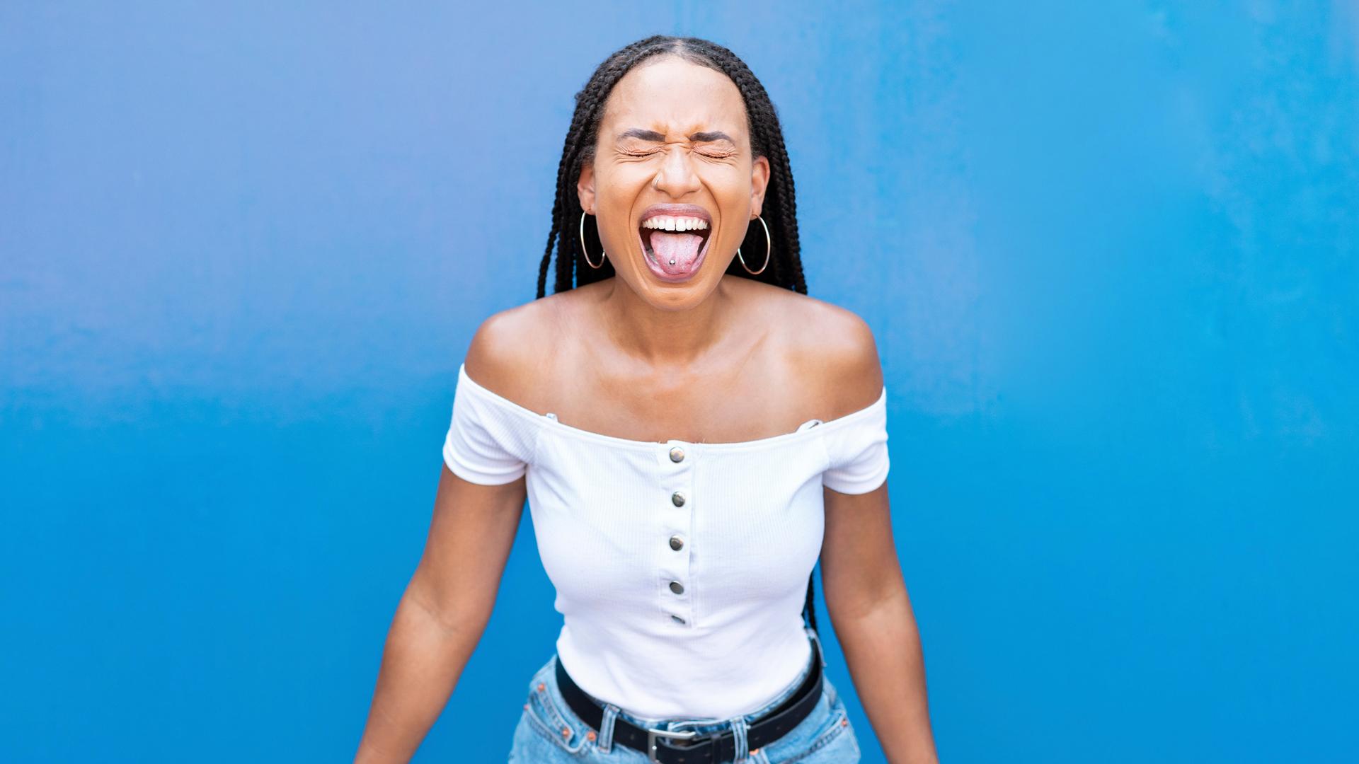 Frau streckt die Zunge vor blauer Wand raus. Frau streckt die Zunge vor blauer Wand raus.