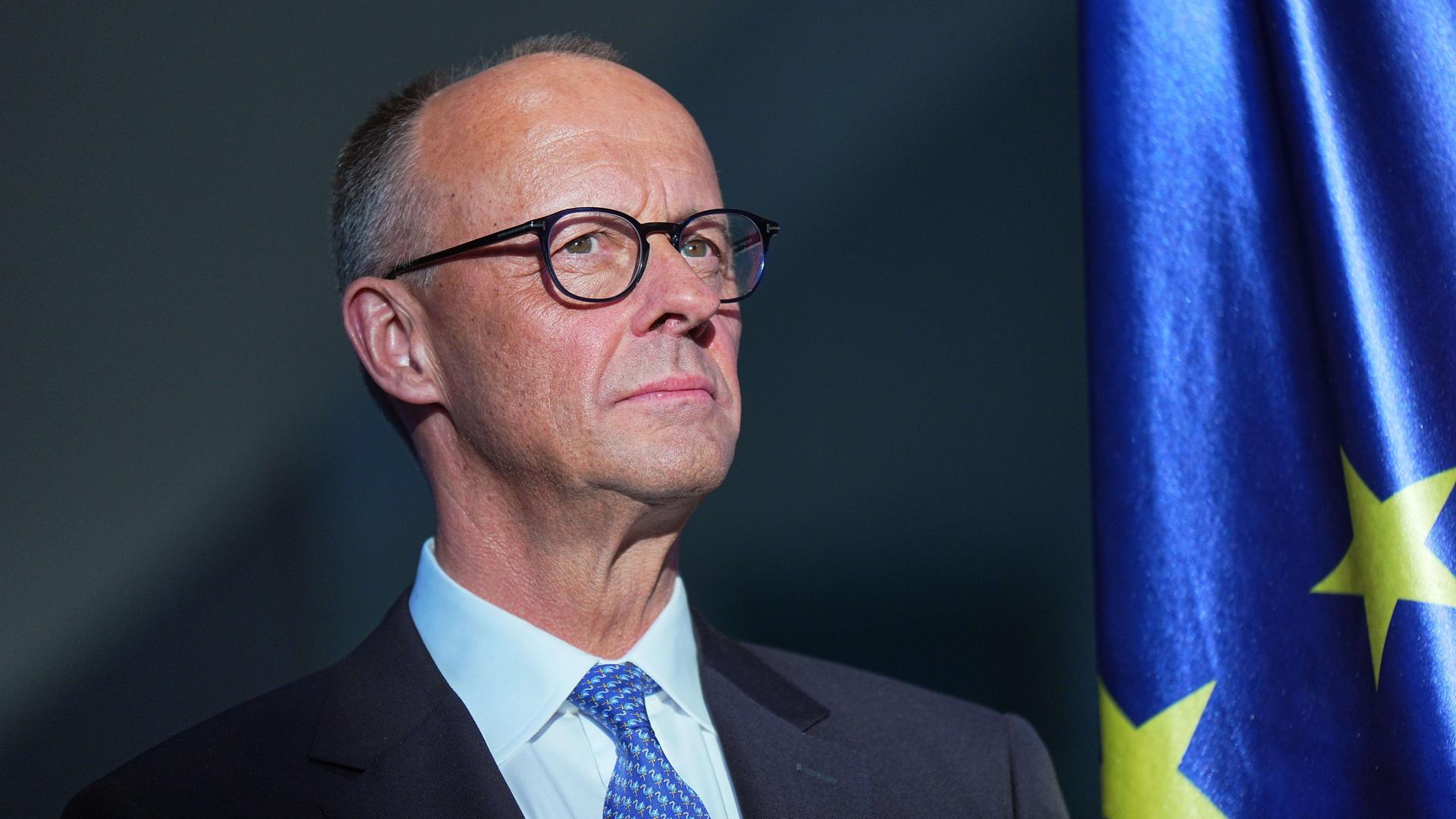Bundeskanzler Friedrich Merz (CDU) während der Amtsübergabe im Kanzleramt, er schaut ernst nach oben, neben ihm ist eine EU-Fahne zu sehen. Bundeskanzler Friedrich Merz (CDU) während der Amtsübergabe im Kanzleramt, er schaut ernst nach oben, neben ihm ist eine EU-Fahne zu sehen.