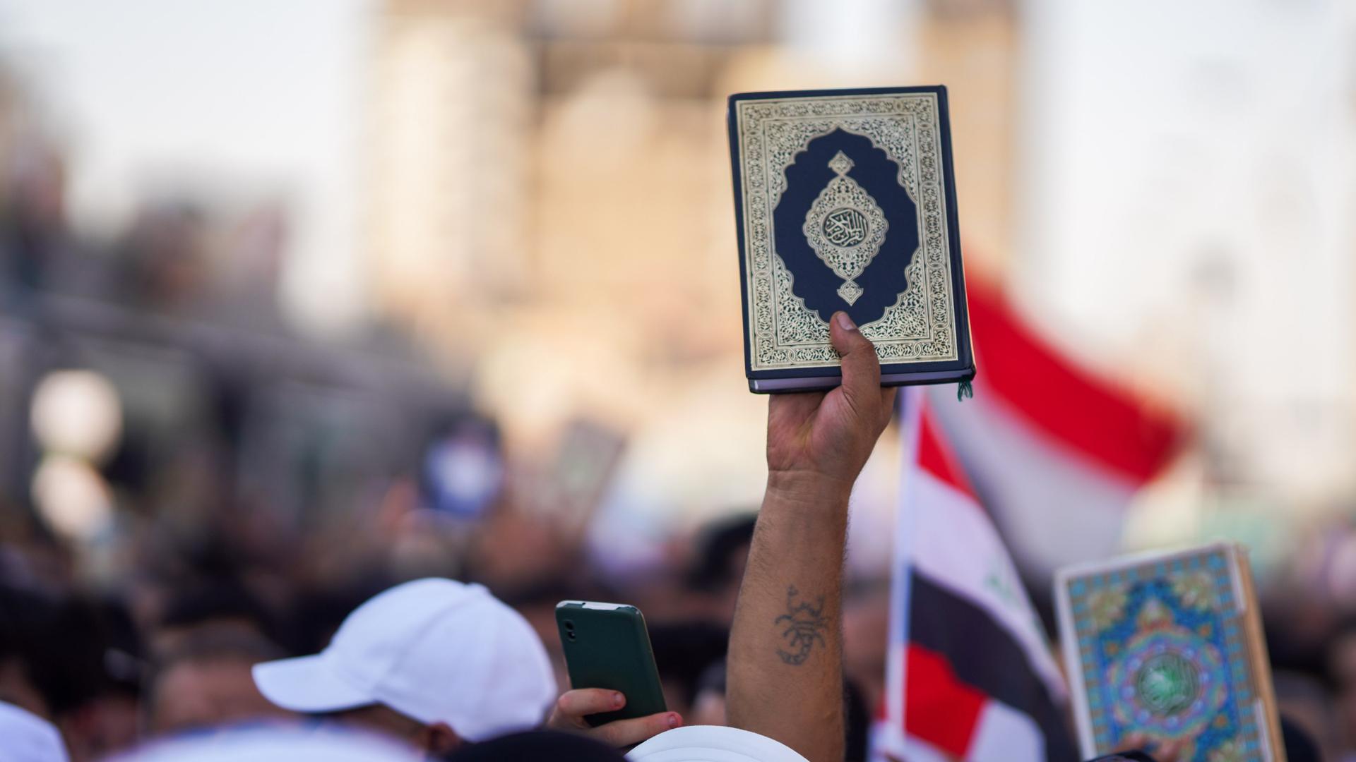 Ein Mann hält einen Koran auf einer Demonstration im Irak nach oben.