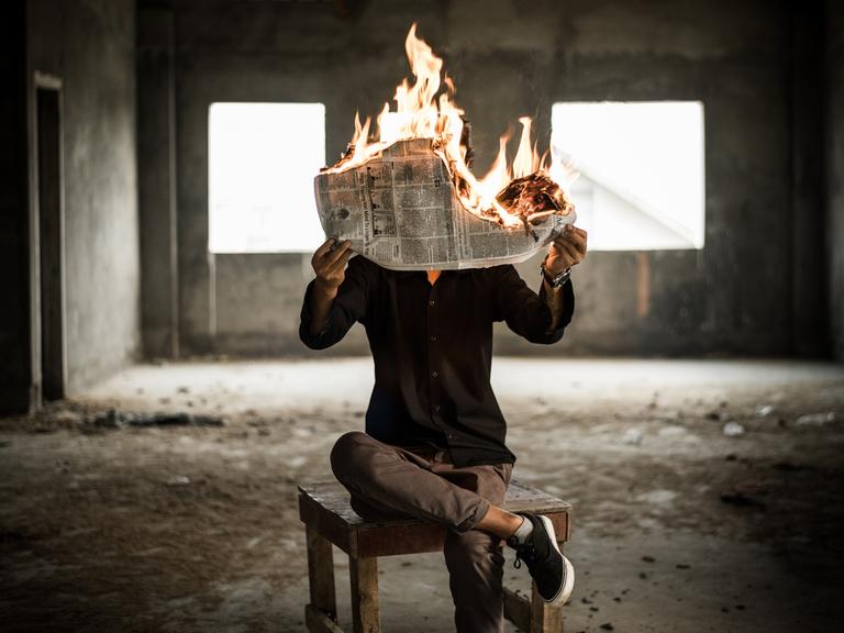 Ein Mann hält eine brennende Zeitung.