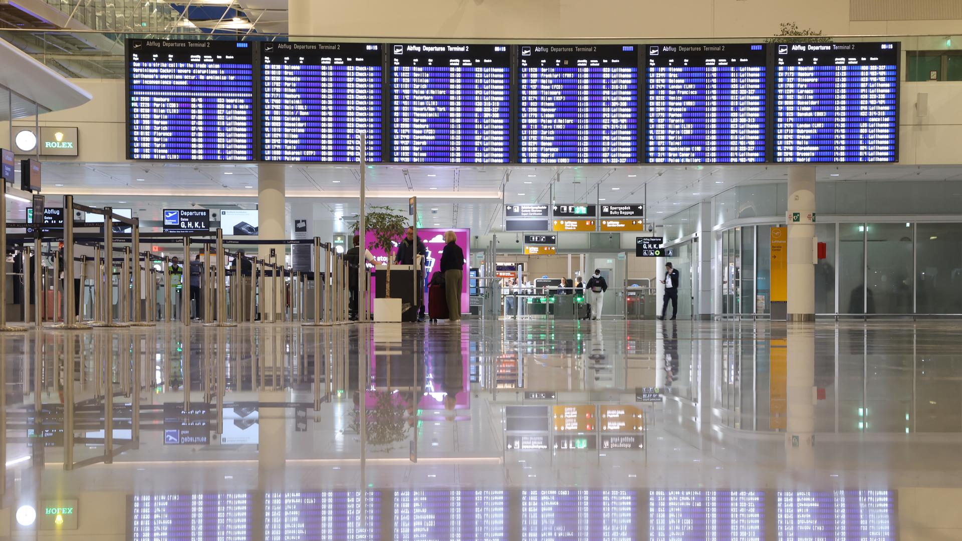 Eine Anzeigetafel spiegelt sich auf dem Boden der leeren Abflughalle eines Flughafens. 