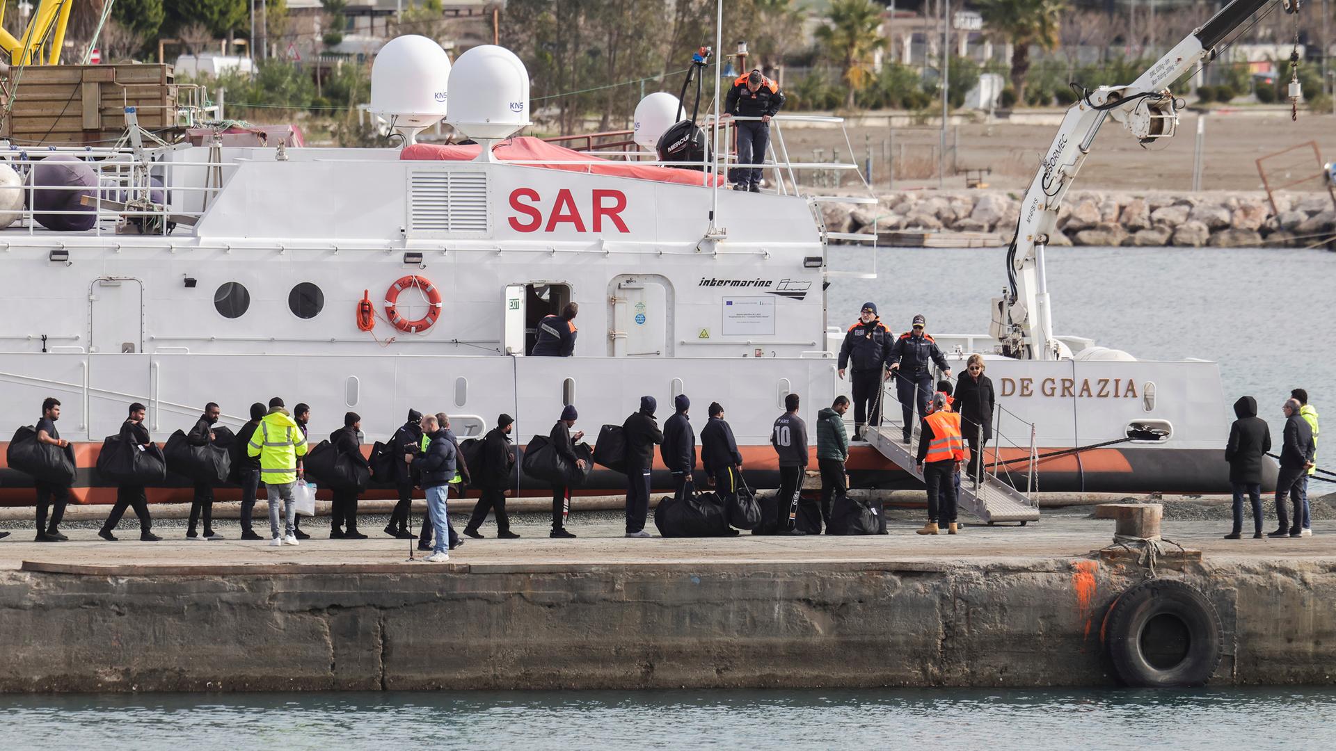 Migranten besteigen ein Schiff der italienischen Küstenwache in enem Hafen in Albanien. 