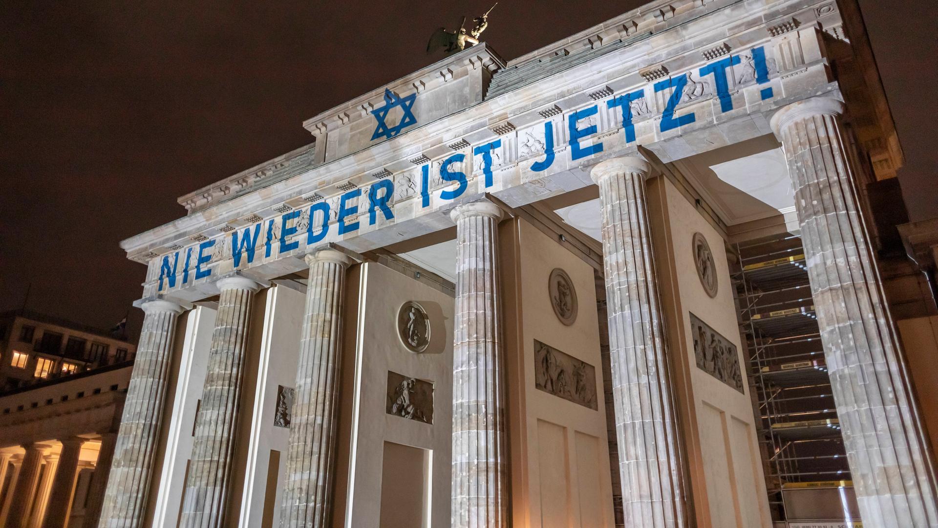 Das Brandenburger Tor ist blau-weiß angestrahlt. Der Schriftzug "Nie wieder ist Jetzt" ist zu lesen. 