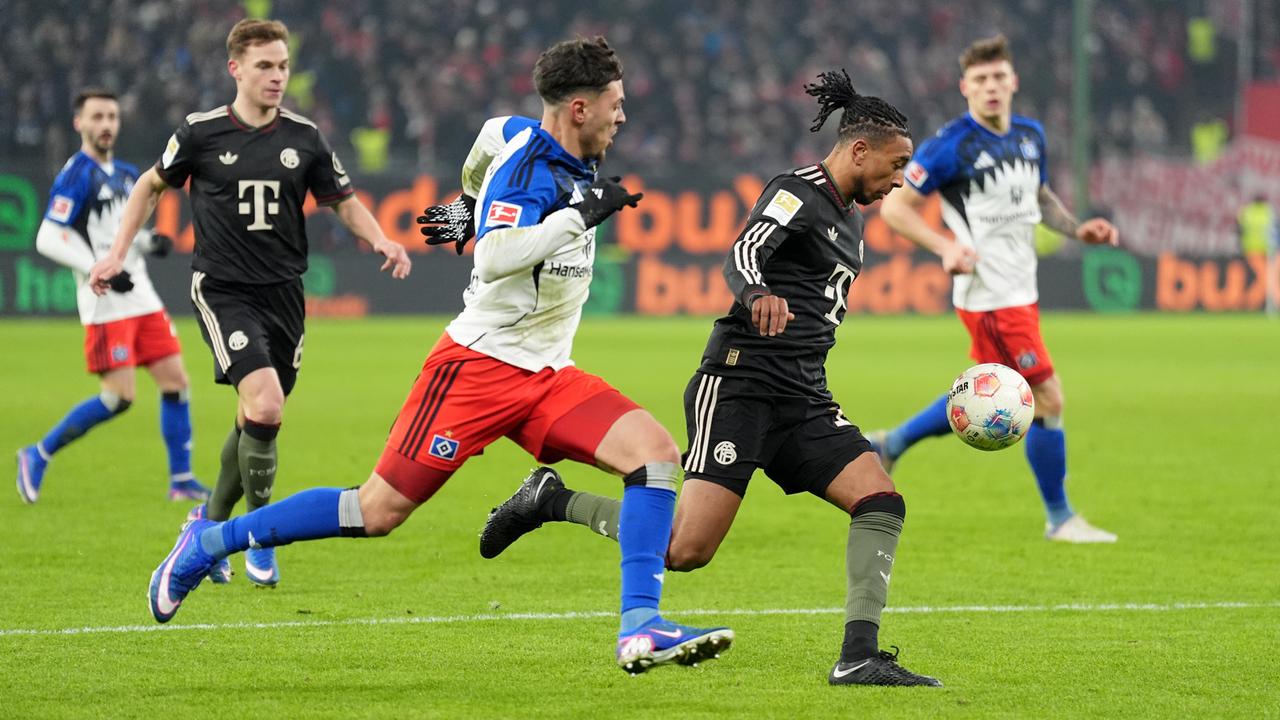 Das Bild zeigt zwei Fußball-Spieler in vollem Lauf beim Kampf um den Ball. In Hintergrund sind Mitspieler zu sehen, die das Geschehen beobachten.