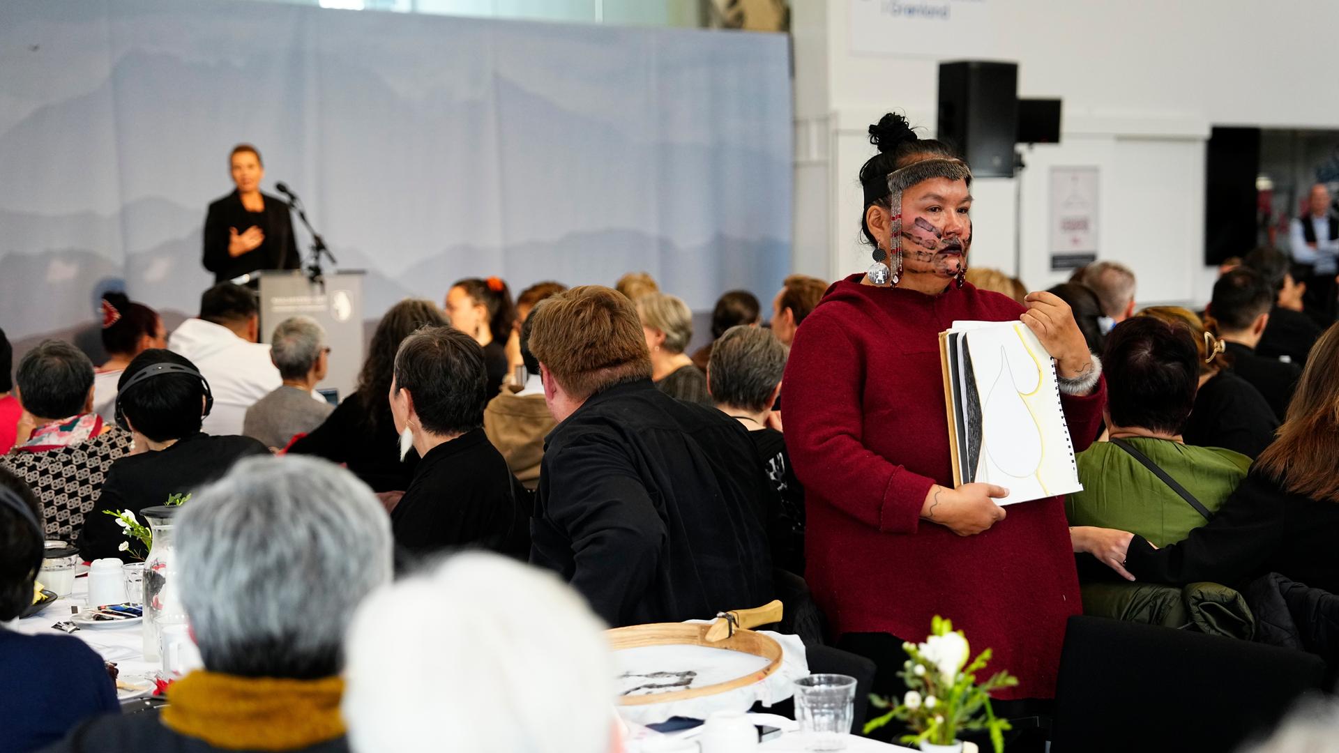 24.09.2025, Grönland, Nuuk: Eine Inuit-Frau steht mit dem Rücken zur dänischen Ministerpräsidentin Mette Frederiksen, während sie während eines Treffens im Kulturhaus Katuaq in Nuuk spricht. 24.09.2025, Grönland, Nuuk: Eine Inuit-Frau steht mit dem Rücken zur dänischen Ministerpräsidentin Mette Frederiksen, während sie während eines Treffens im Kulturhaus Katuaq in Nuuk spricht.