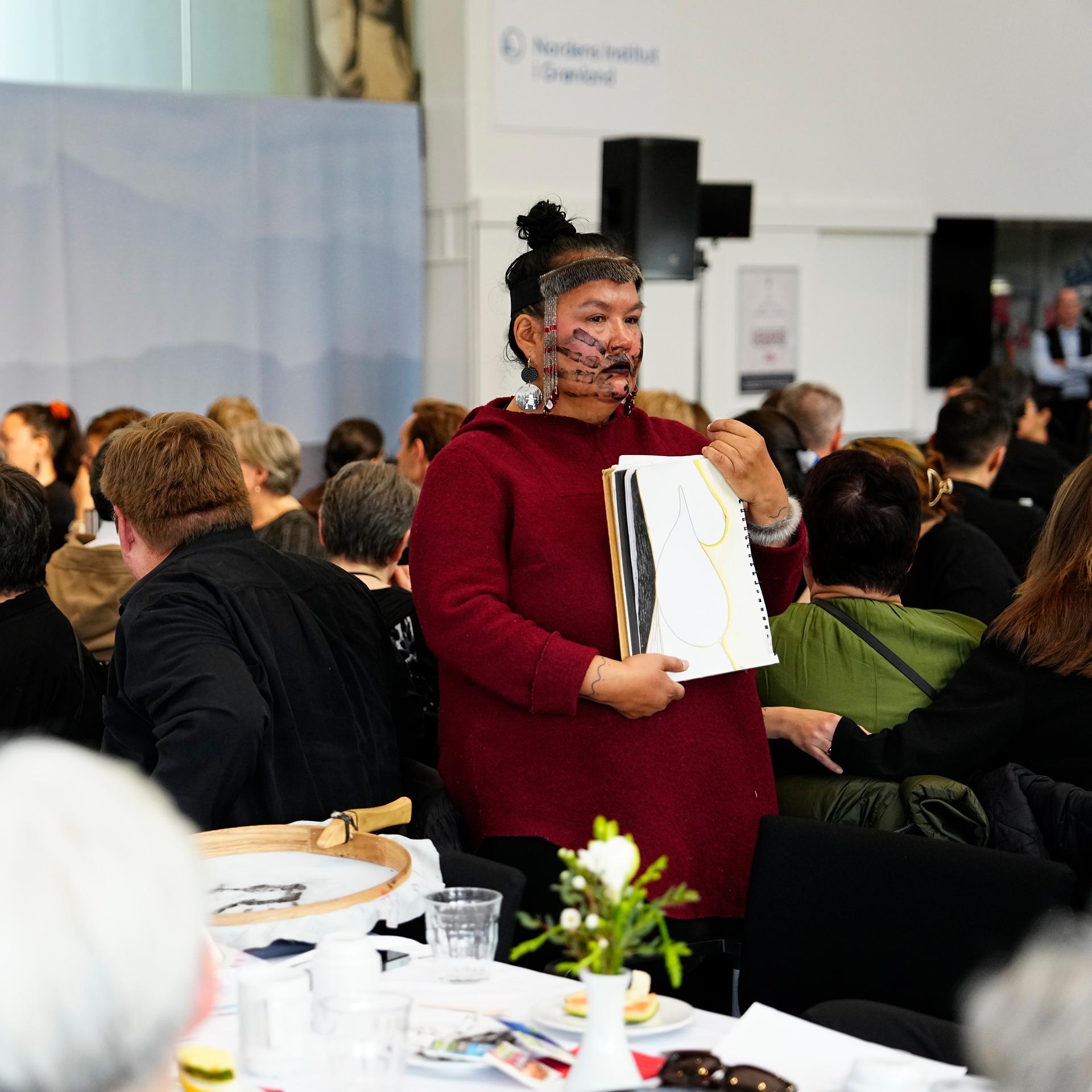 24.09.2025, Grönland, Nuuk: Eine Inuit-Frau steht mit dem Rücken zur dänischen Ministerpräsidentin Mette Frederiksen, während sie während eines Treffens im Kulturhaus Katuaq in Nuuk spricht.