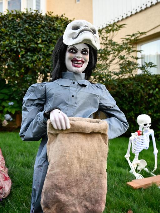 Gruselige Figuren auf einem Rasen vor einem Haus.