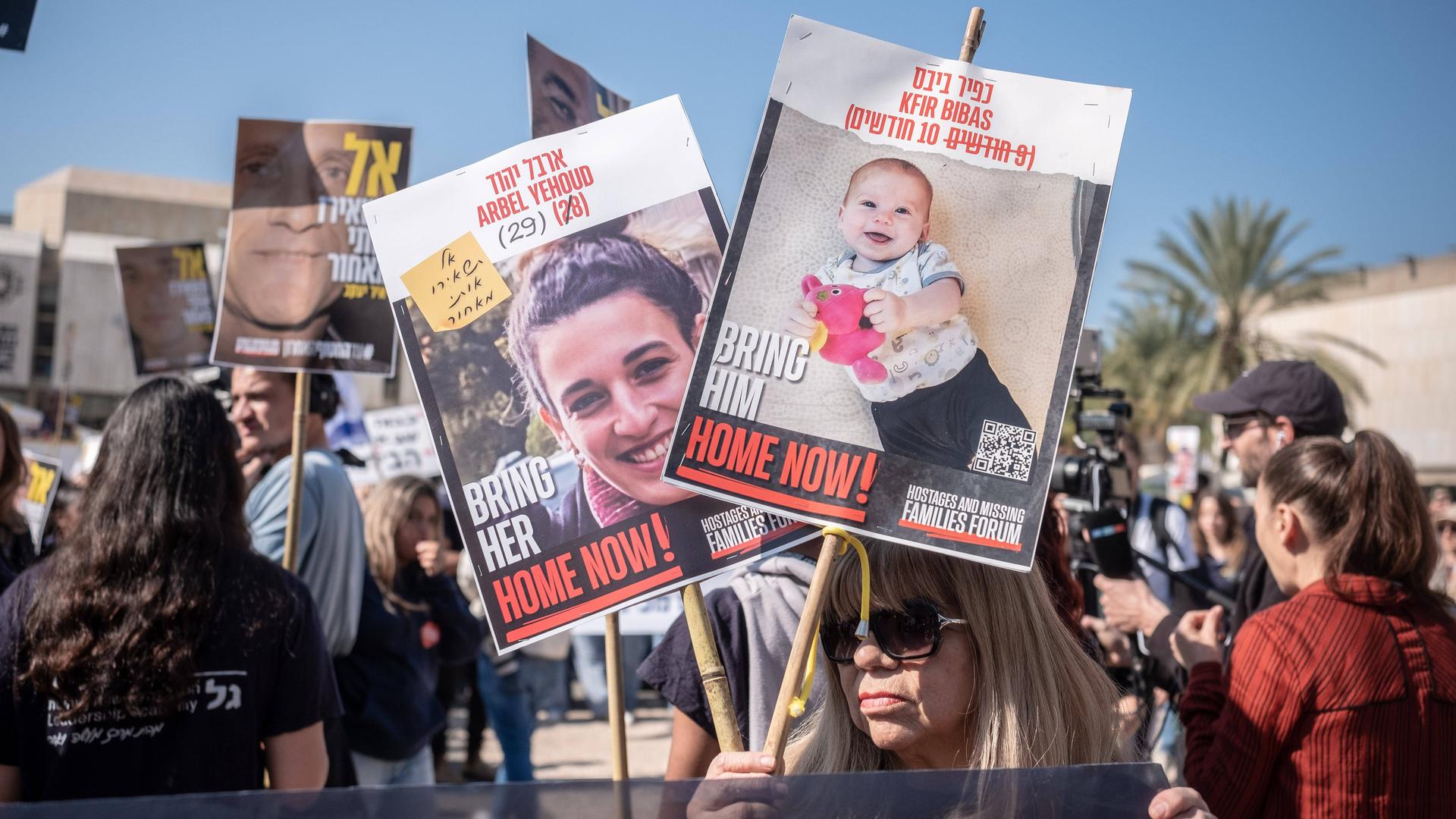 Das Foto zeigt eine Frau mit Plakaten. Darauf sind Fotos von Geiseln, die die Hamas entführt hat. 