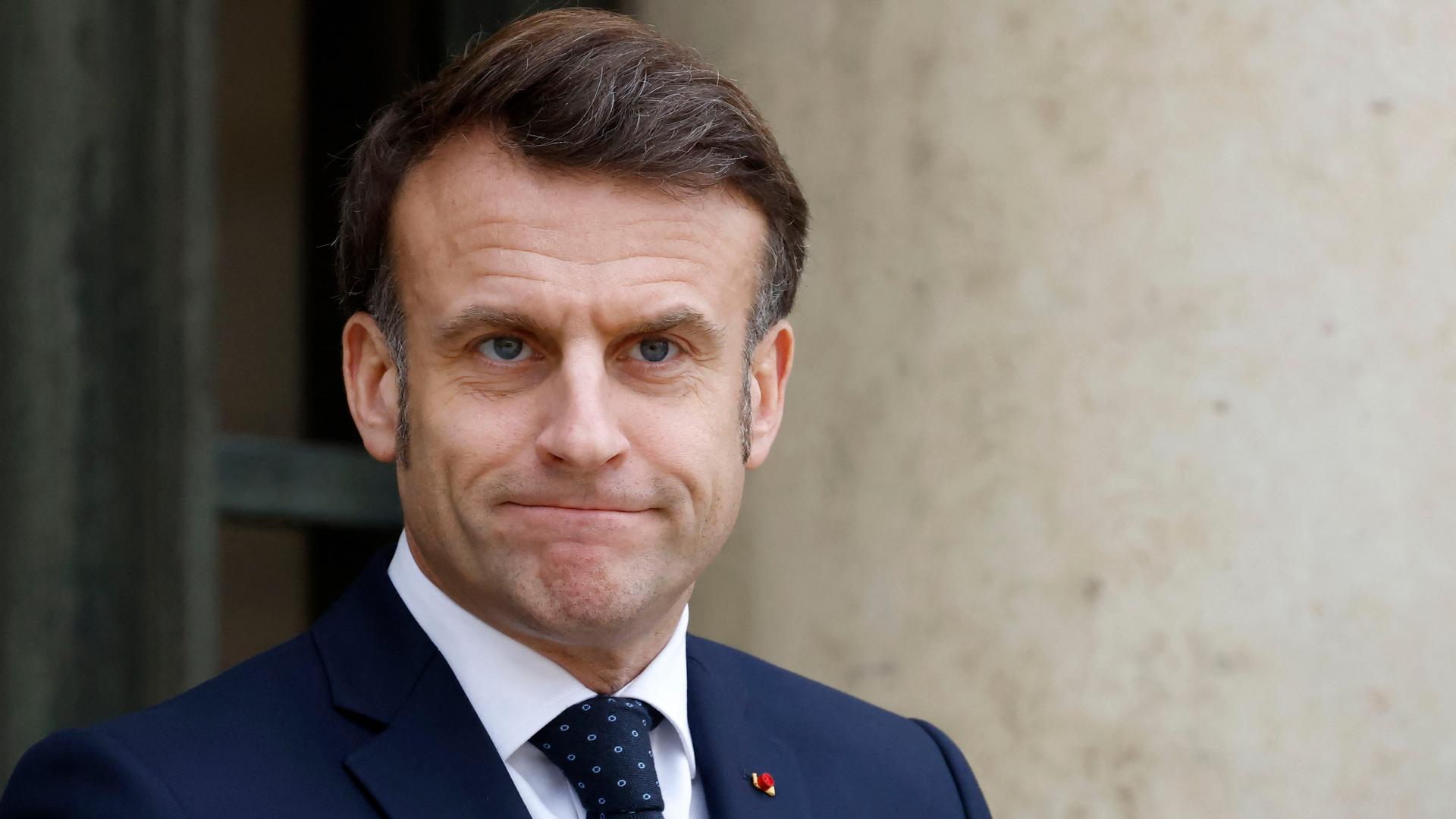 Frankreichs Präsident Emmanuel Macron in Nahaufnahme. Er trägt einen blauen Anzug mit Krawatte. Er presst die Lippen aufeinander und lächelt leicht.