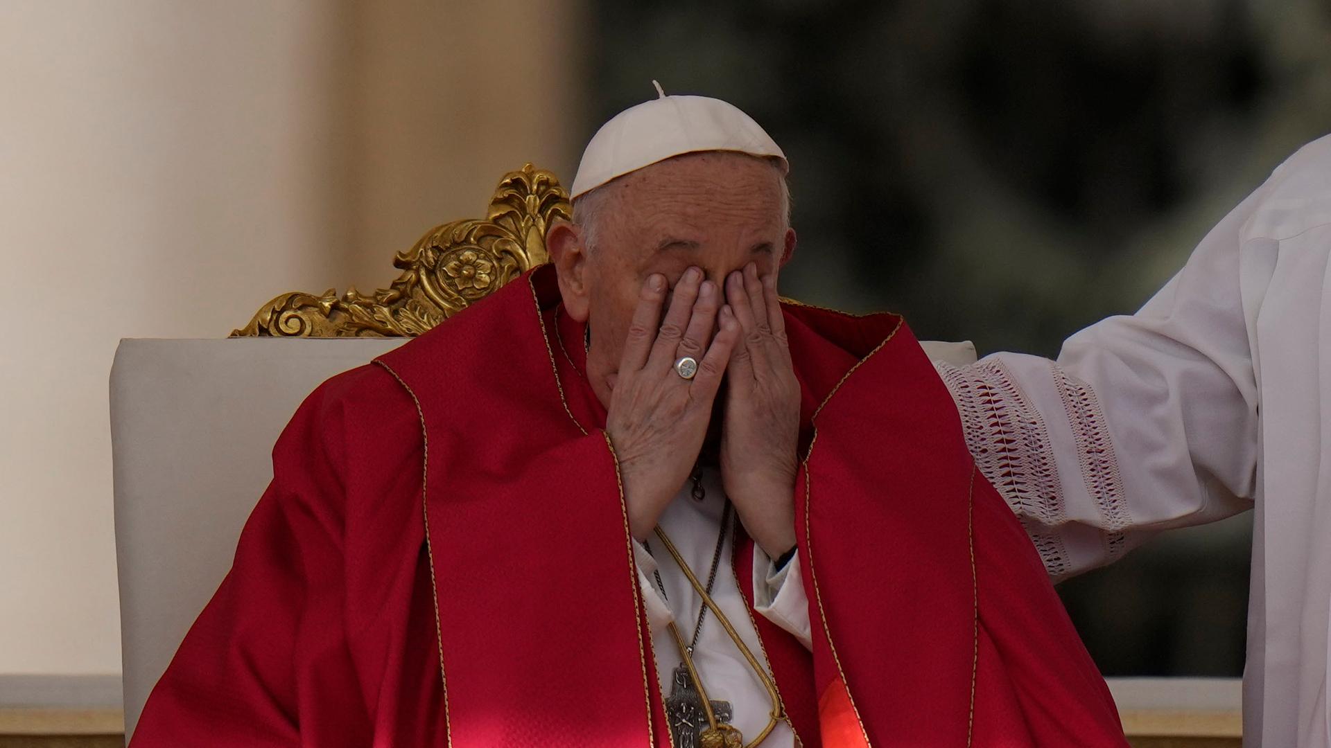 Das Bild zeigt Papst Franziskus während der Palmsonntagsmesse auf dem Petersplatz in Rom. Der Papst hält das Gesicht mit seinen Händen bedeckt.