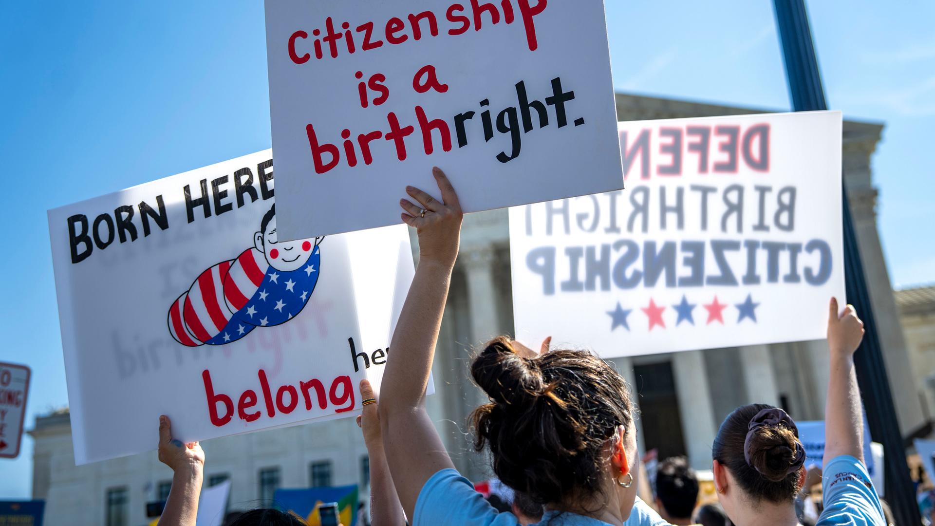 Mehrere Menschen stehen vor dem Supreme Court in Washington und halten Plakate in die Höhe. 