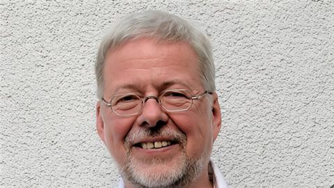 Walter Thomas Heyn lacht in die Kamera, während er seine Gitarre bei sich hat.