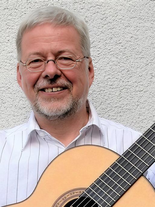 Walter Thomas Heyn lacht in die Kamera, während er seine Gitarre bei sich hat. Walter Thomas Heyn lacht in die Kamera, während er seine Gitarre bei sich hat.