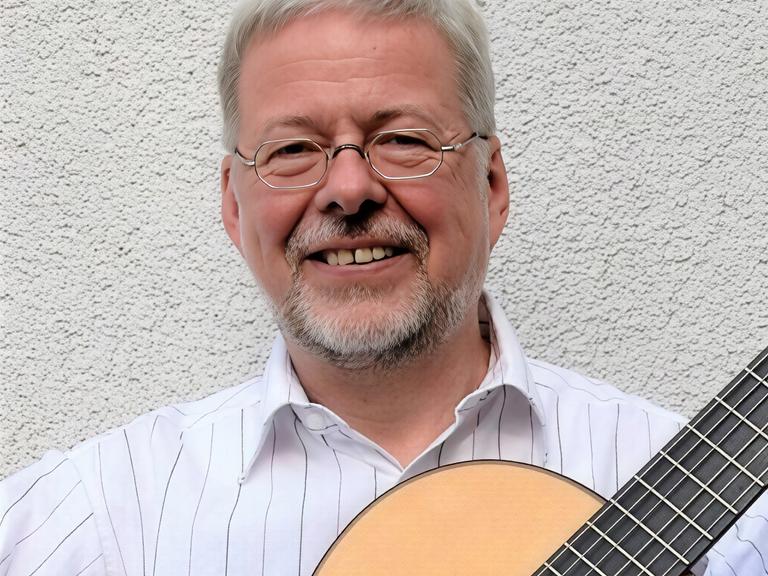 Walter Thomas Heyn lacht in die Kamera, während er seine Gitarre bei sich hat. Walter Thomas Heyn lacht in die Kamera, während er seine Gitarre bei sich hat.
